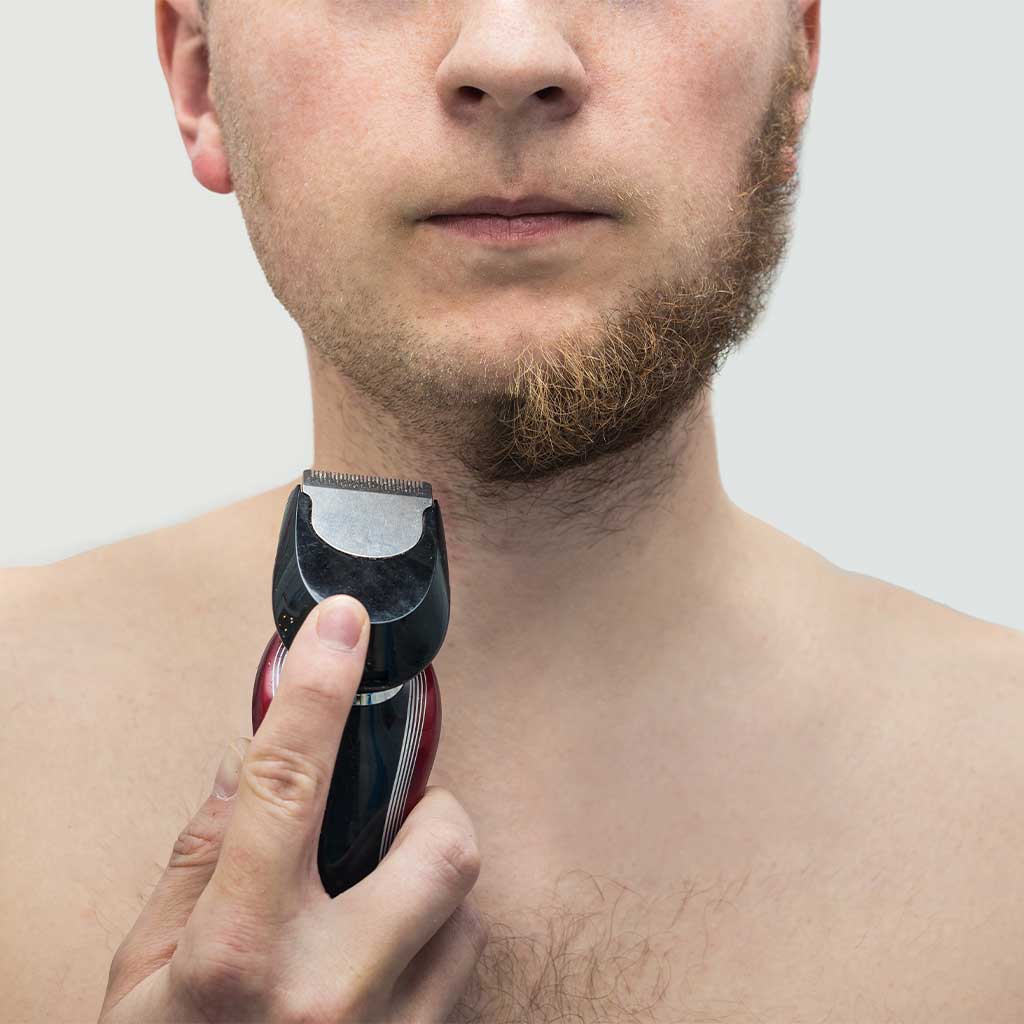 Mašinica za brijanje u ruci čovjeka na pola obrijanog.